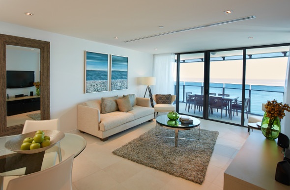  a room with a white sofa, glass centre table, gray carpet and a huge sliding glass door with an ocean view outside