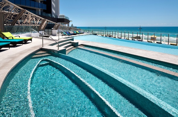  a geometric pool near the ocean with bright green and blue lounge chairs on the side 