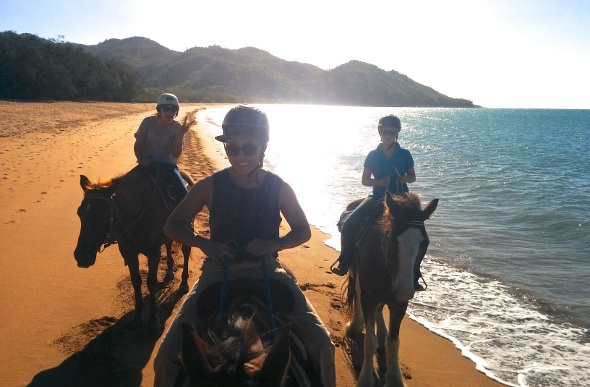 Three people riding horses along the shore