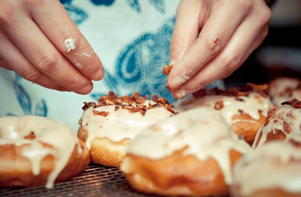 A person sprinkling a tasty and crunchy nuts in a glazed Doughnuts 