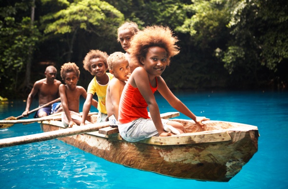 Kids sitting in a canoe over the blue water of Nanda Blue Hole