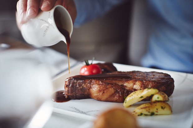 A passenger pouring gravy over a steak 