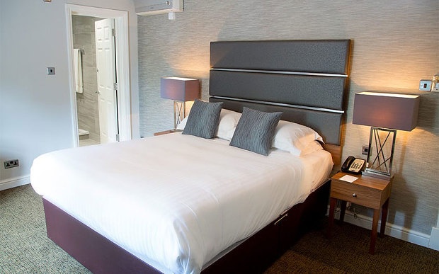 Black and white double bed in hotel room next to two purple lamps