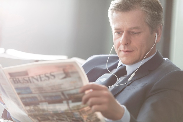 A businessman reading a newspaper with headphones on