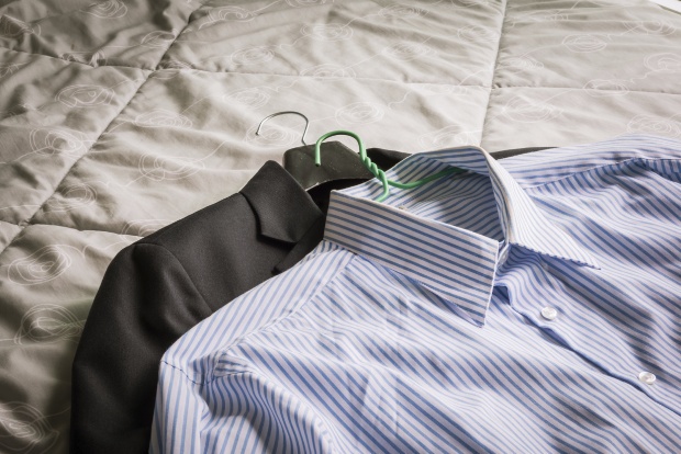 Collared shirt and a suit on a hanger are laid on a bed