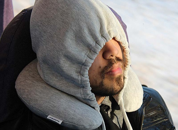 Man wearing a grey hoodie over his eyes using a grey travel neck pillow 