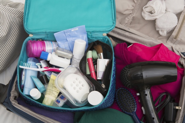 Open blue toiletries bag in a suitcase with a hair dryer, hair brush and clothes. 