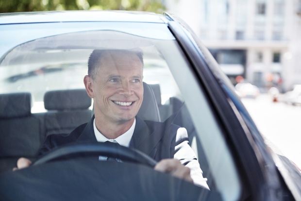 Man in suit driving while looking out the window smiling