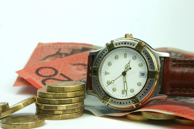 Close-up shot of a wristwatch next to some twenty-dollar bills and coins