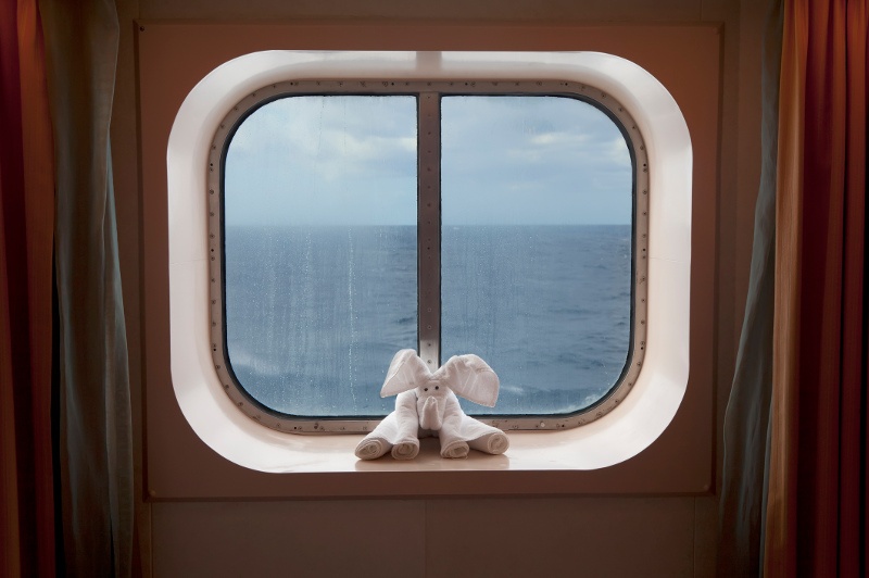 A towel-art elephant sits on a window sill in a cruise ship cabin.