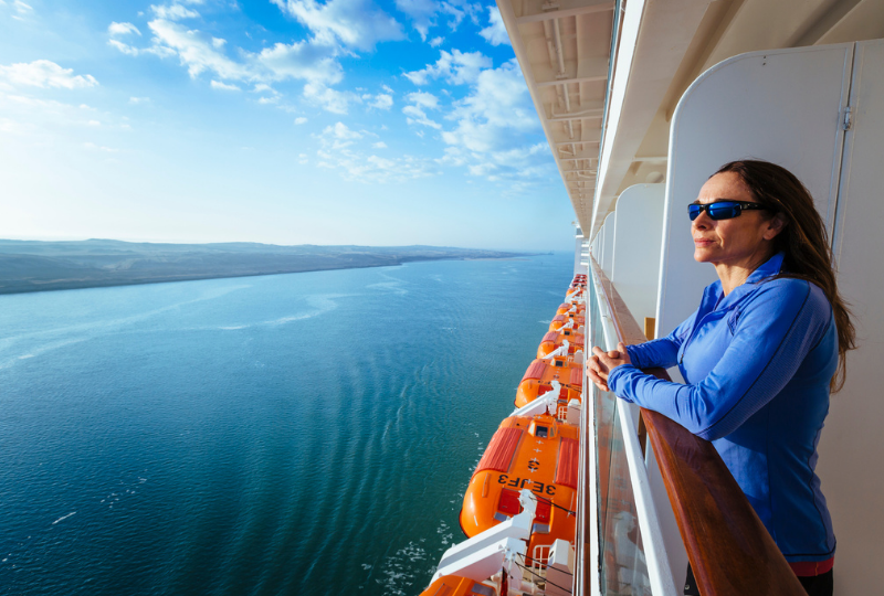 a woman with black shades and blue cardigan looking out the cruise ship deck