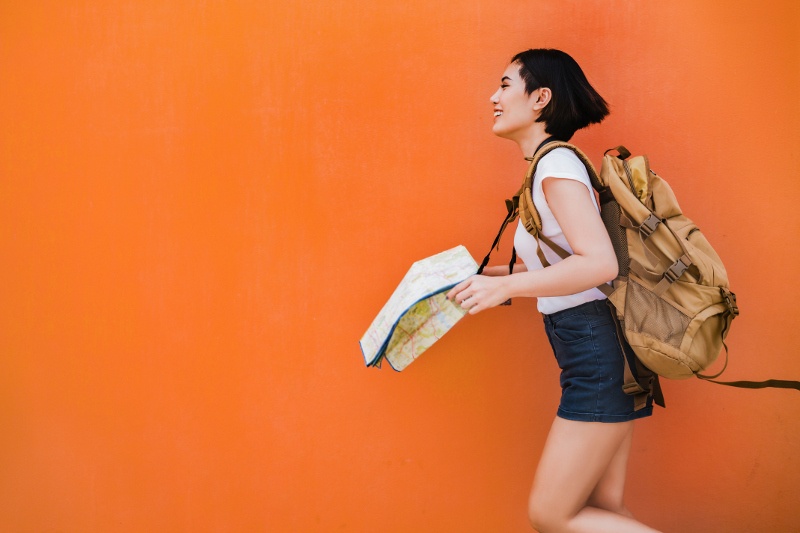 woman standing behind orange wall with map and backpack 