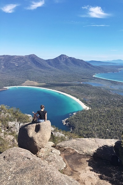 A lady sitting on top of the stone looking at the perfect view of the mountain and the sea. 