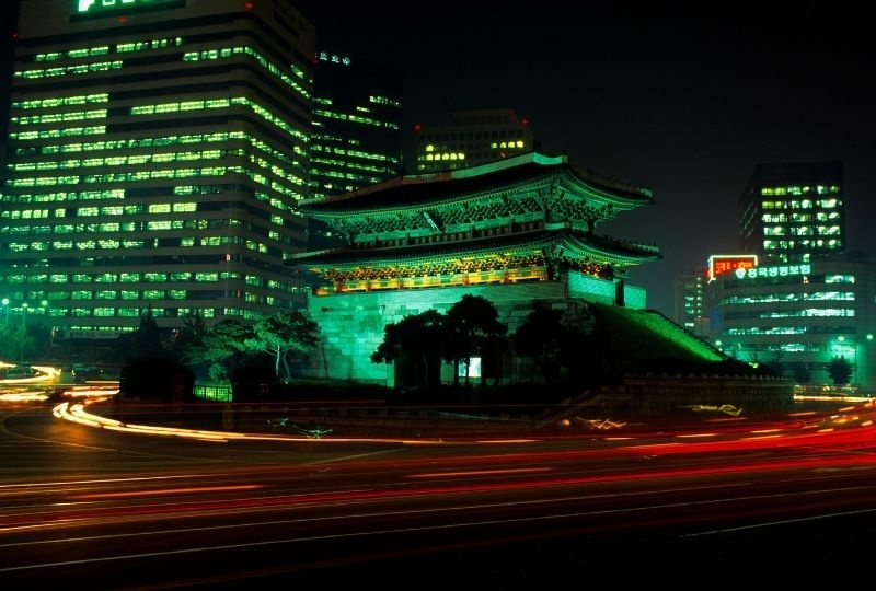 one of the right city gates lit with green lights at night with office buildings surrounding
