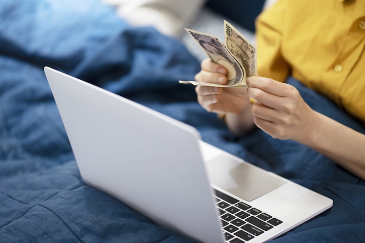 Woman holding money as she uses her laptop 