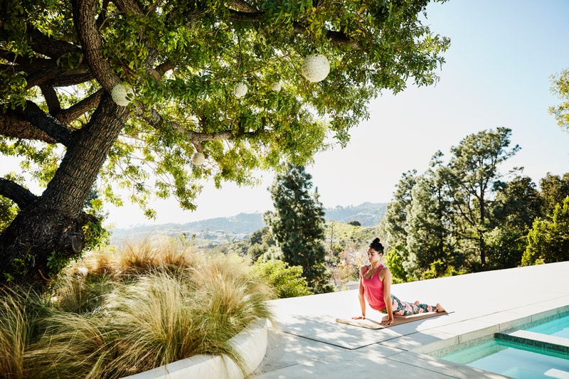 Woman in pink singlet practicing yoga next to pool and trees
