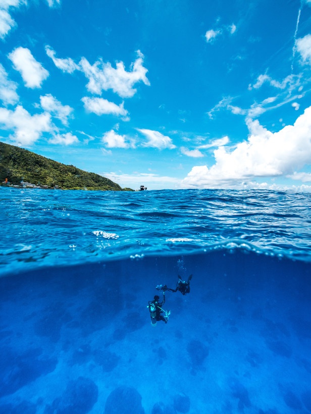 divers under water with view of ocean and mountains above