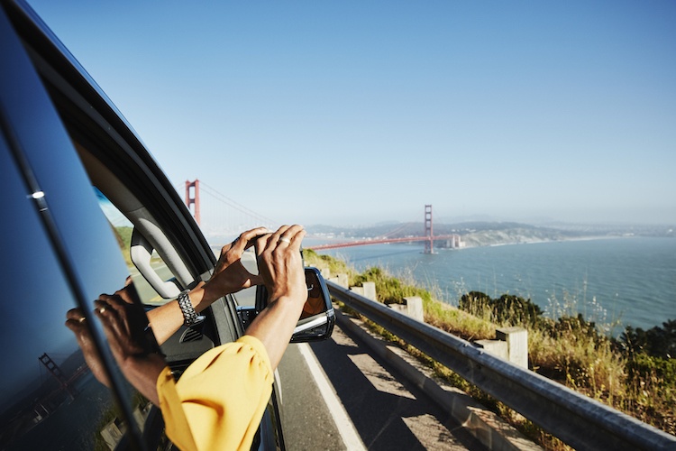 Woman leaning out the car window taking a photo of the Golden Gate Bridge 