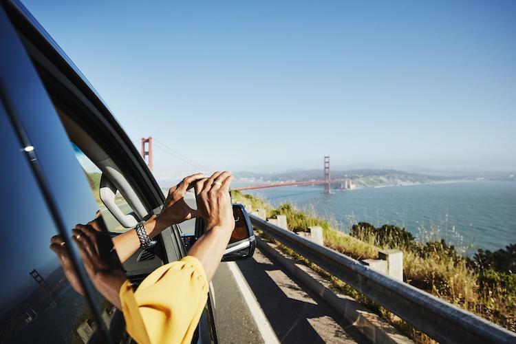 Woman leaning out the car window taking a photo of the Golden Gate Bridge