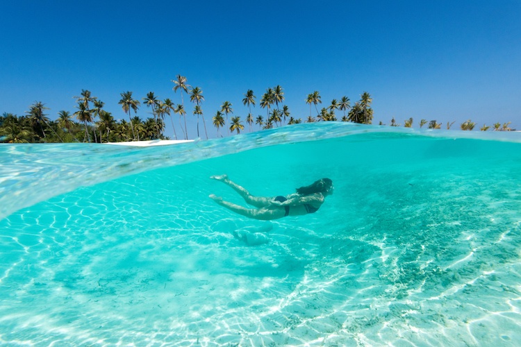 Woman in a black bikini swimming through crystal clear blue water 