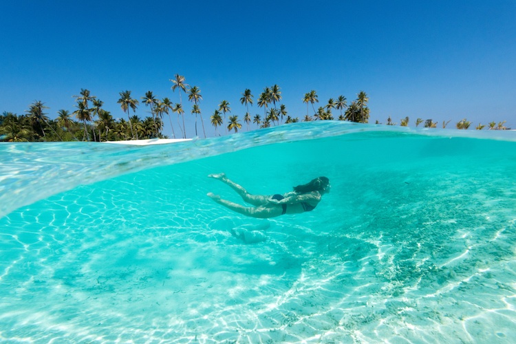 Woman in a black bikini swimming through crystal clear blue water