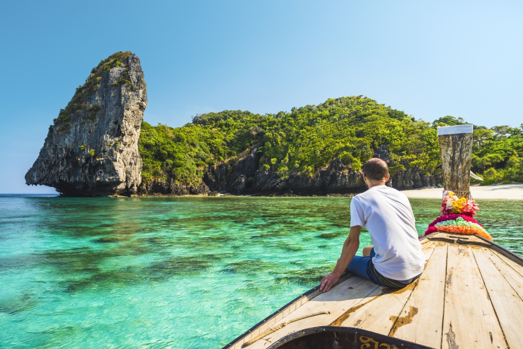 A guy riding a wooden boat with a flower on the boat going towards an island