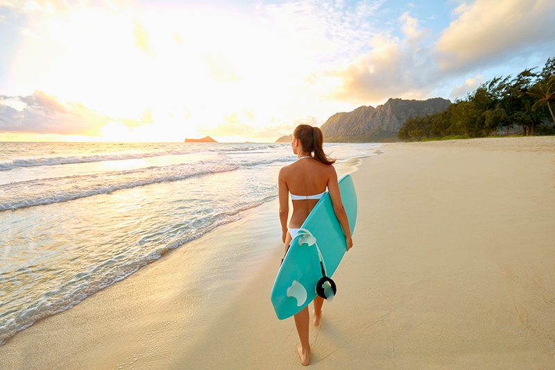 Woman carrying surfboard on Hawaii beach