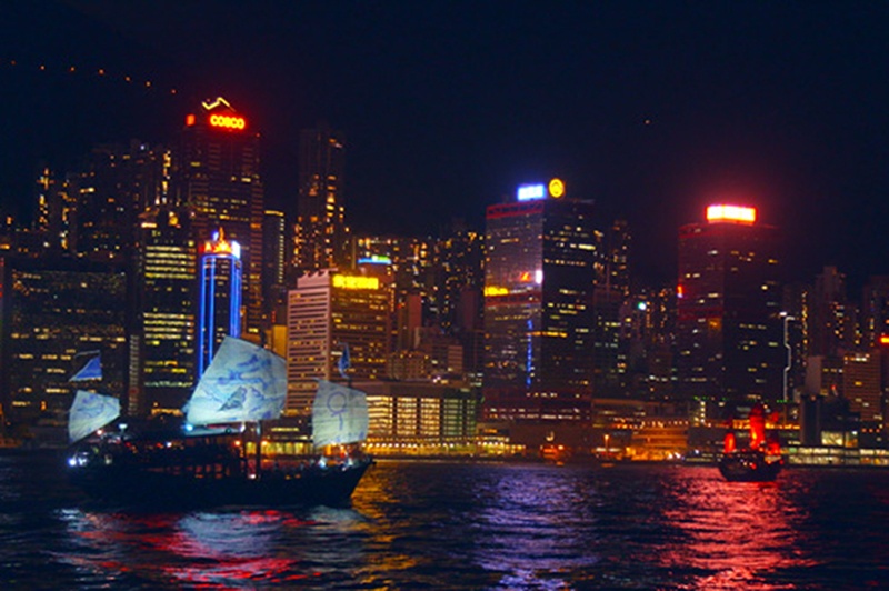 A junk boat cruises Hong Kong's Victoria Harbour amid the sparkling night-time lights.