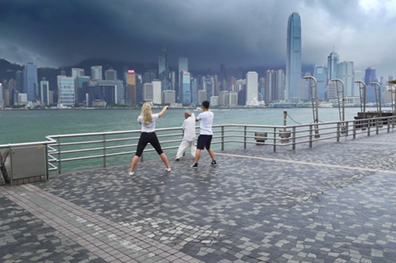 Three people practise tai chi by the harbour in Hong Kong.