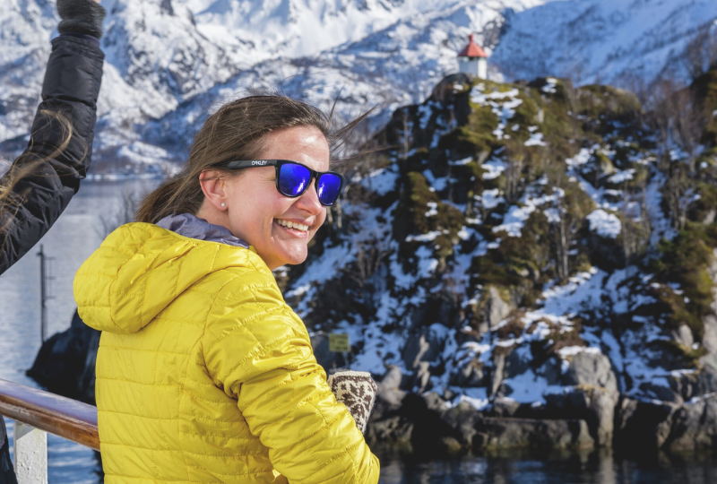 a woman in yellow jacket and blue shades smiling while looking at the snowy scenery
