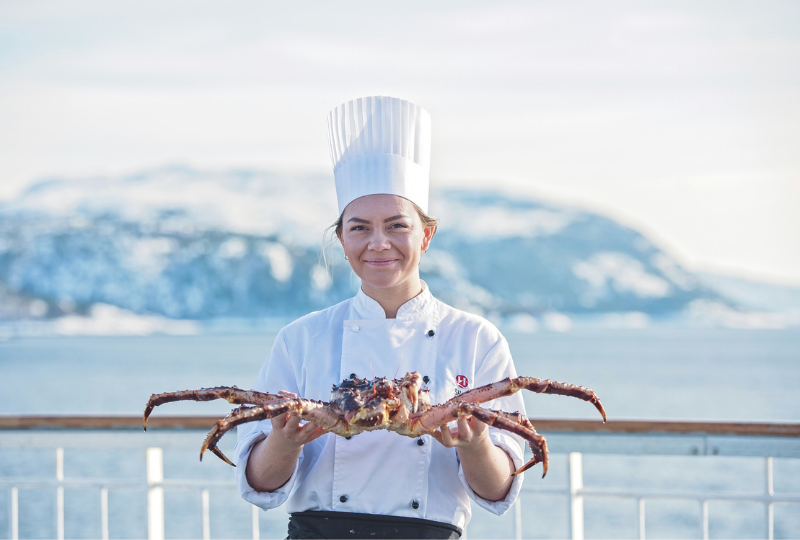 Lady Chef showing a huge king crab with a mountain in her background