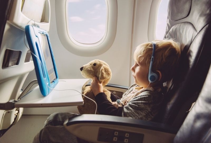 Image of a young kid watching a movie of a plane while holding a teddy bear