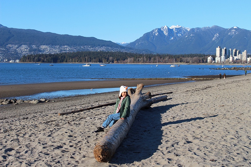 Girl sits on log at Kitsilano Beach, Vancouver