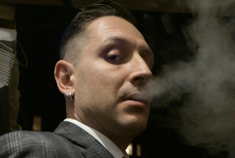 a guy in plaid suit looking at the camera while blowing smoke from his mouth