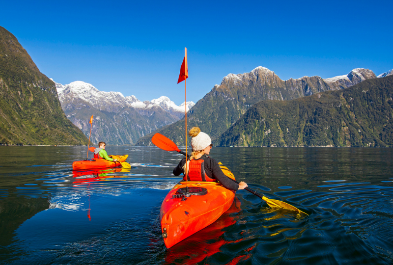 two tourists enjoying the orange kayak on a lake between mountains
