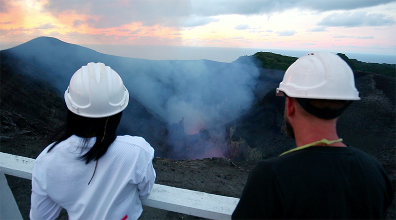 People wearing safety hats observing an active volcanic crater