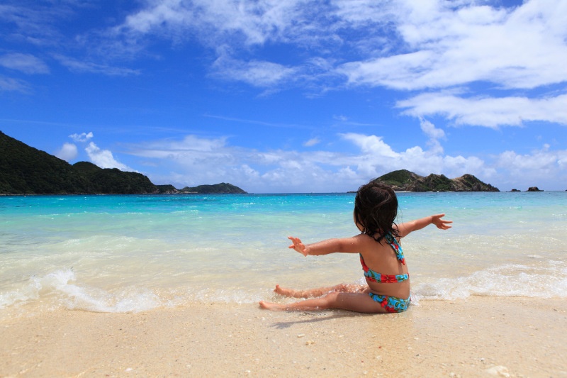 A child sits on the sand, stretching out her arms, at a beach in Okinawa's Kerama Islands.