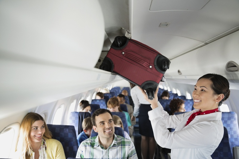 Flight attendant putting suitcase in overhead compartment