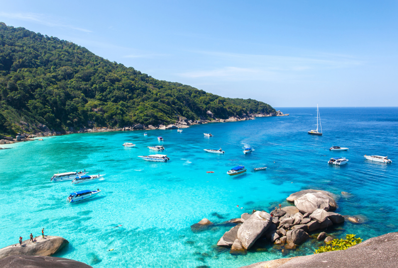 A view of the beach filled with yacht, boats, and people enjoying the sun