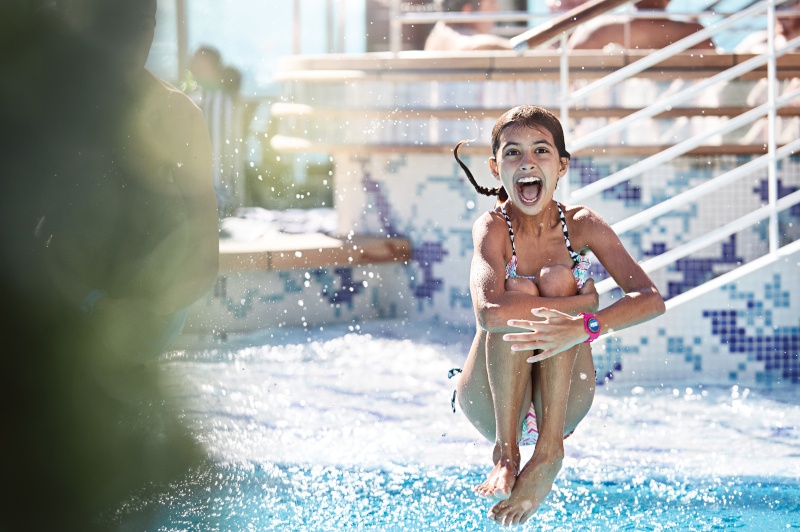 A kid jumping into the pool on board. She is wearing a medallion as a wrist band