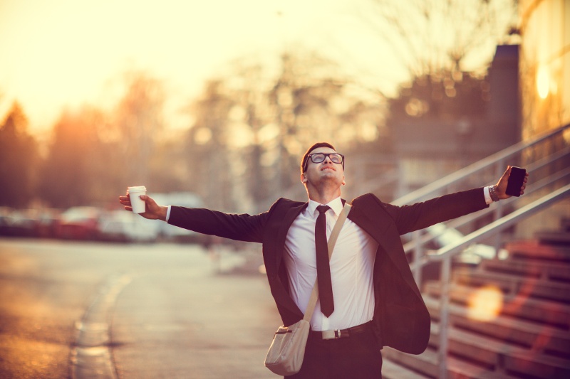 A businessman stands with arms outstretched in a city street.