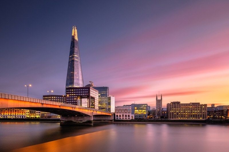 Sunset shot of the London bridge with the city buildings with lights