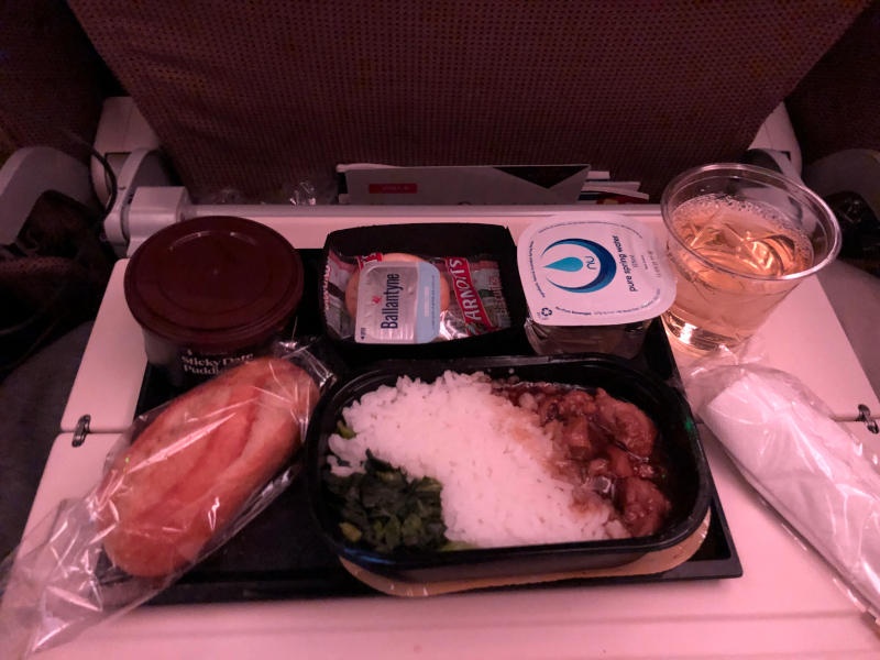 A photo of an economy class meal. Chicken curry with rice, white wine, bread and a pudding