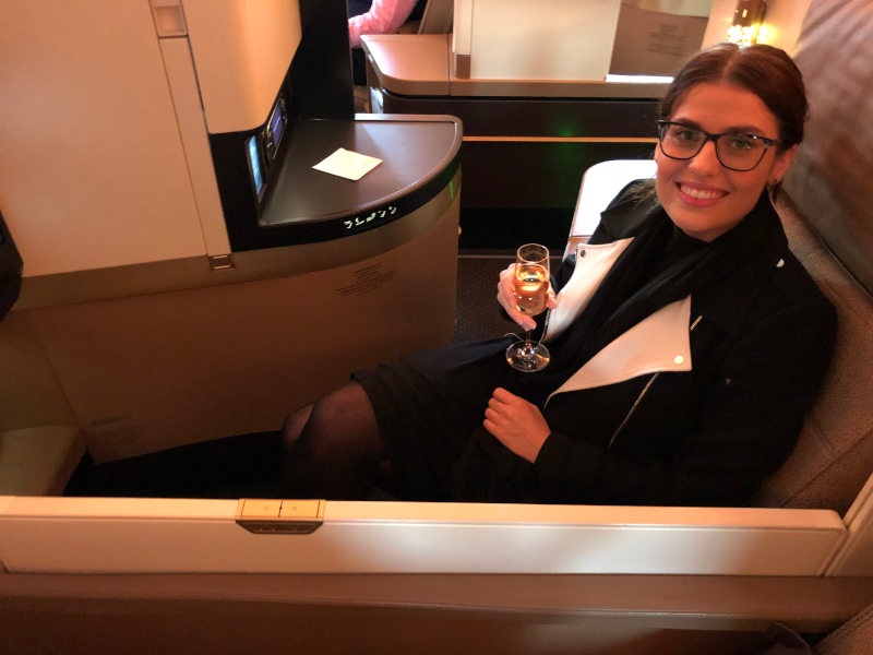 Woman sitting in a business class seat holding champagne and smiling