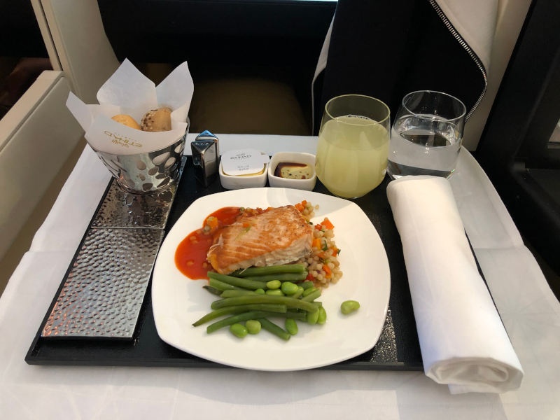A photo of a meal in business class. Salmon with green beans, champagne and also bread. 