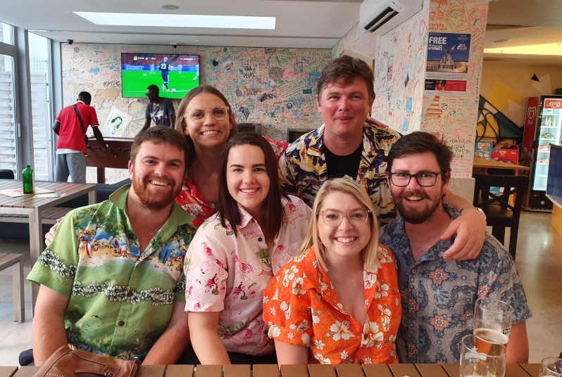 A group of six people looking at the camera and smiling. They are wearing matching hawaiian shirts