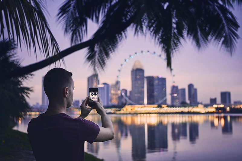 Man taking photo of Singapore cityscape with smartphone at night.