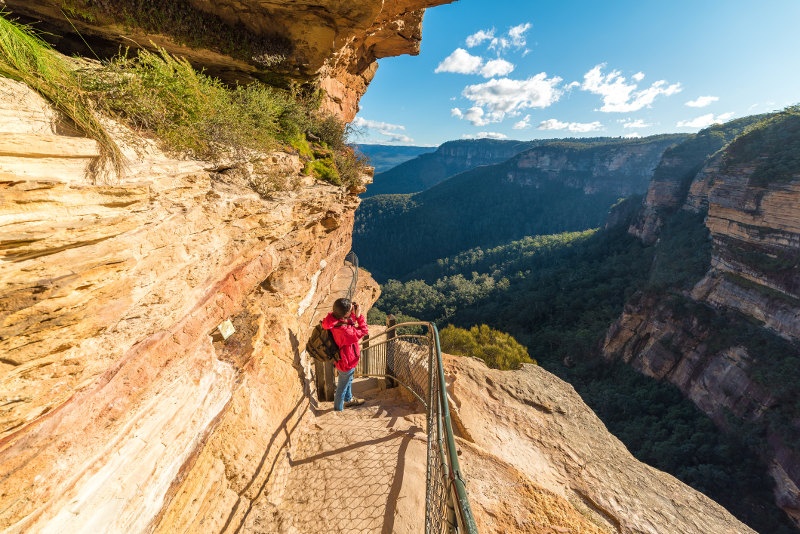 A hiker takes a photo on a trail that skirts sandstone bluffs in New South Wales' Blue Mountains.