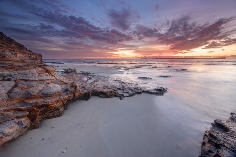 Sunrise over sand, sea and rocks at Jervis Bay, New South Wales.