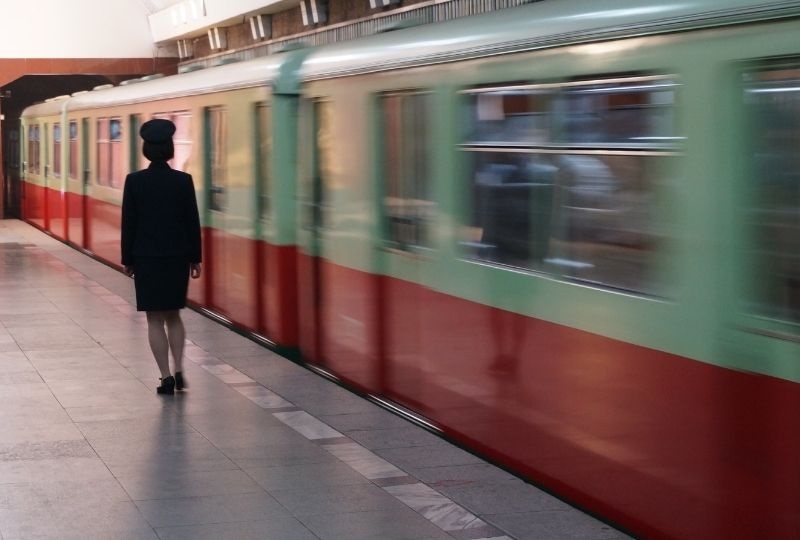 femme presenting person in uniform walking on train platform as train goes past 